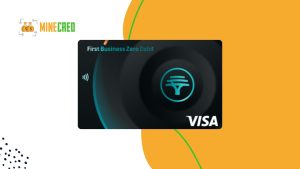A black FNB First Business Zero Debit (FNB Solopreneur Bundle) Visa card with a glowing teal logo in the center and contactless icon, set against a white and orange abstract background with the MineCred logo in the top left corner.