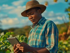 A small farmer in a plaid shirt and straw hat uses a digital tablet in a crop field under a blue sky, illustrating modern finance tools for small farmers.