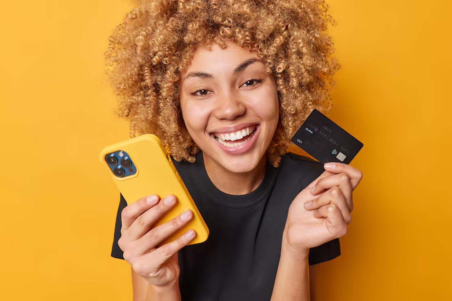 Smiling woman holding a smartphone and a black prepaid card, representing financial empowerment through prepaid cards.