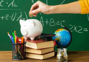 A piggy bank on books beside a graduation cap, globe, and jar of coins, symbolizing education loans and financial planning for students.