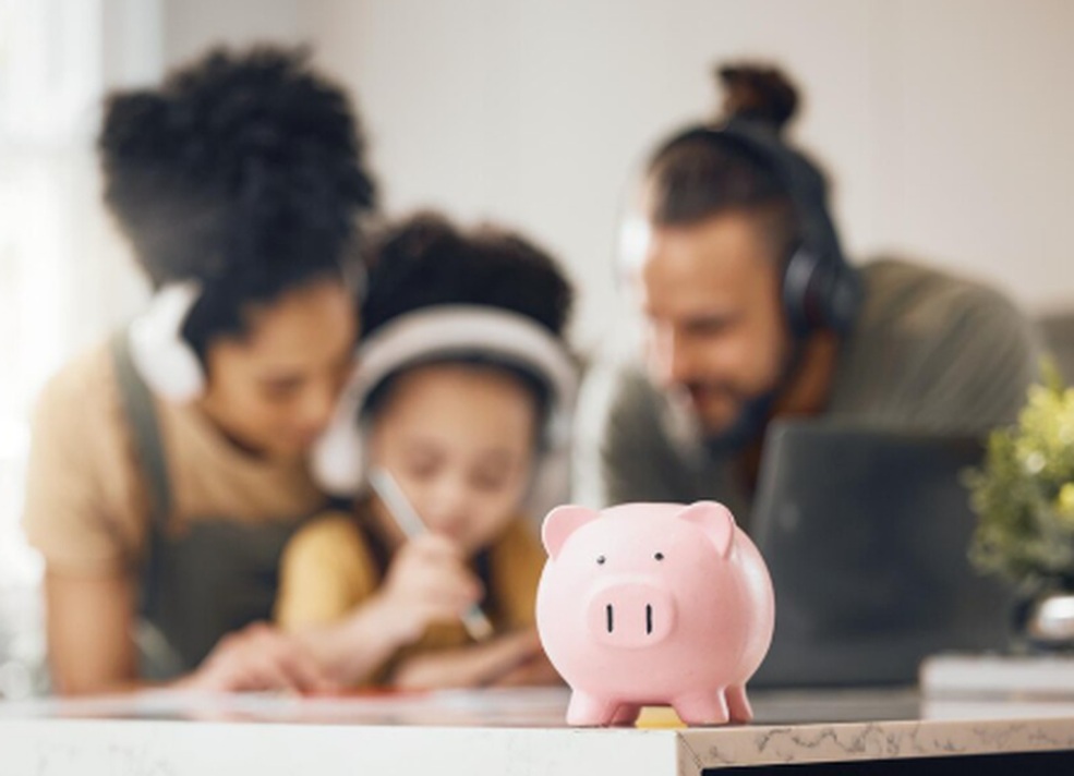 A pink piggy bank on a table with a family in the background planning their family budget together at home.