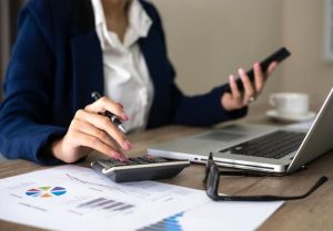 Young entrepreneur calculating expenses with laptop and charts on the desk, demonstrating smart money management and the importance of sustainable finances when starting a business.