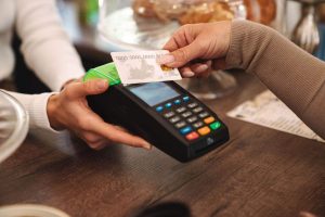 A customer pays using a contactless card reader in a café, showing how credit cards with local rewards support everyday purchases like dining and small businesses.