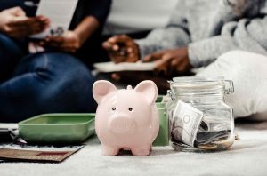 Pink piggy bank next to a glass jar filled with cash and coins, symbolizing savings and financial planning in everyday family life.
