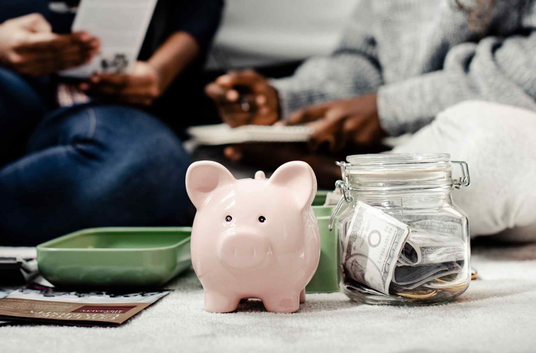 Pink piggy bank next to a glass jar filled with cash and coins, symbolizing savings and financial planning in everyday family life.