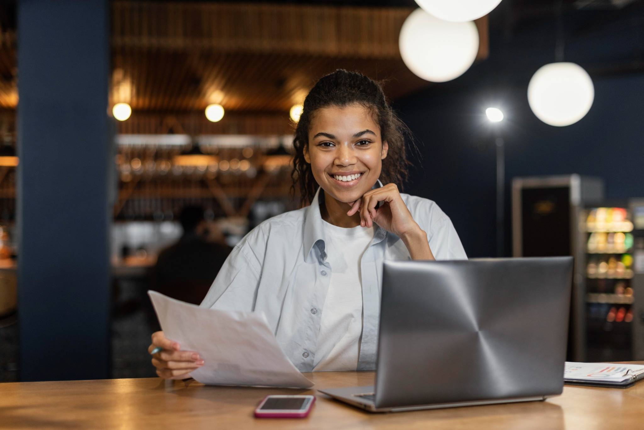 Smiling young entrepreneur reviewing documents and working on a laptop in a modern workspace, representing the use of loans for small market vendors to support the growth of local small businesses.